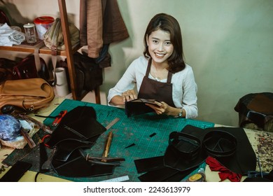 Smiling craftswoman holding pieces of tanned leather while making a leather jacket pattern