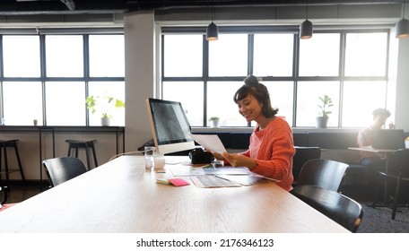 Smiling Creative Asian Businesswoman Looking At Photograph At Computer Desk In Office. Unaltered, Creative Business, Workplace, Photography Themes.