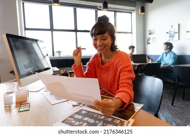 Smiling Creative Asian Businesswoman With Photograph At Computer Desk In Office. Unaltered, Creative Business, Workplace, Photography Themes.