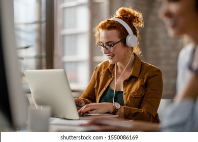 Smiling creative businesswoman listening music on headphones while working on a computer in the office.  - Powered by Shutterstock