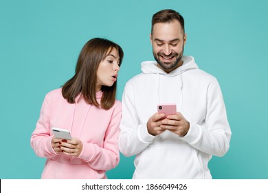 Smiling Curious Young Couple Two Friends Man Woman 20s Wearing White Pink Casual Hoodie Using Mobile Cell Phone Typing Sms Message Isolated On Blue Turquoise Colour Wall Background Studio Portrait