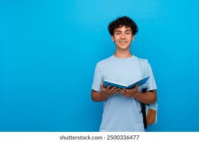 Smiling curly boy guy high school male pupil student teenager with bag holding open books copybooks isolated on blue background copy space for advertisement. Education back to school concept - Powered by Shutterstock