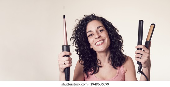 Smiling Curly-haired Young Man Can't Decide Between Using His Curling Iron Or His Hair Straightener. Care And Beauty Concept Copy Space.