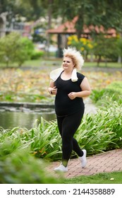 Smiling Curvy Young Woman Jogging In Park On Sunny Day