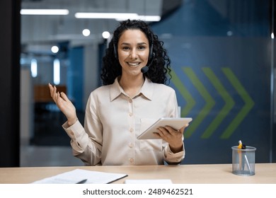 Smiling customer service representative wearing headset holding tablet in modern office environment. Professional woman ready to assist clients. Concept of support, technology, communication - Powered by Shutterstock