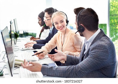 Smiling customer support workers communicating to solve client's problem together at call centre office. Positive hotline operators with headsets having conversation at workplace