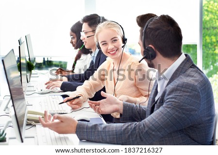 Smiling customer support workers communicating to solve client's problem together at call centre office. Positive hotline operators with headsets having conversation at workplace