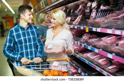 Smiling customers with trolley choosing meat in supermarket