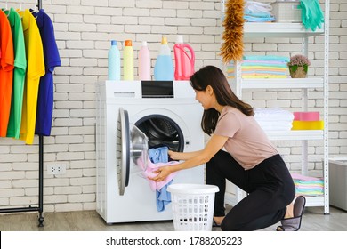 A Smiling And Cute Asian Woman Carrying A Laundry Basket And Posing Beside The Washing Machine. Picking Up Clothes In The Washing Machine. There Are Empty Shelves And Clothes Racks.