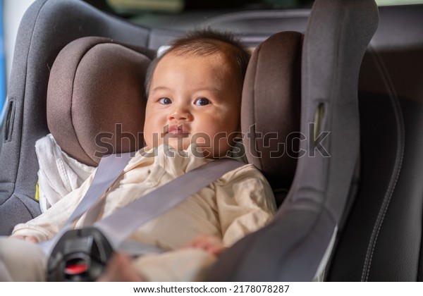 Smiling cute baby sit in car seat and secure with\
safety belts. Happy Asian infant baby sit in baby seat on car and\
looking around in car comfort and cheerful. Baby safety on car seat\
concept