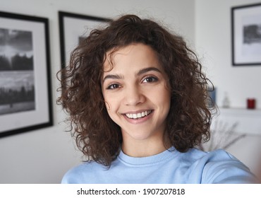 Smiling cute cheerful young pretty hispanic latin woman looking at camera standing alone at home. Happy positive beautiful 20s girl female model posing indoors, close up face headshot portrait.