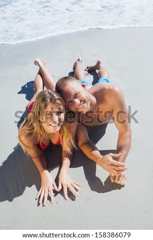 Smiling cute couple in swimsuit posing on the beach looking at camera