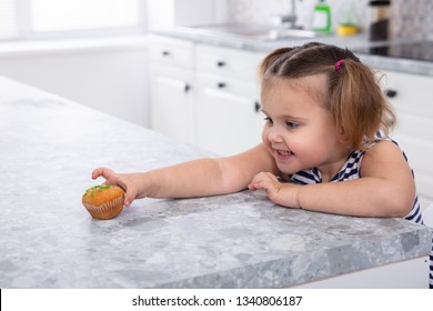 Smiling Cute Girl's Hand Reaching For Cupcake On Kitchen Counter