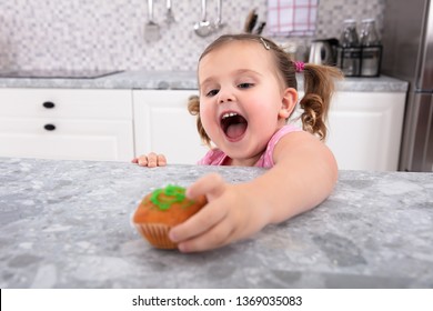 Smiling Cute Girl's Hand Reaching For Cupcake On Kitchen Counter