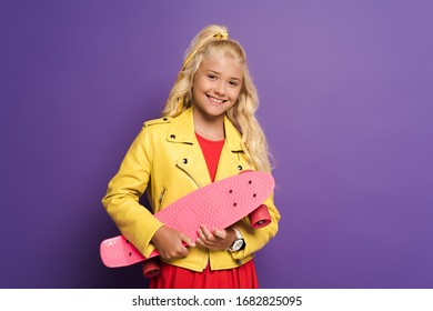 Smiling And Cute Kid Holding Penny Board On Purple Background