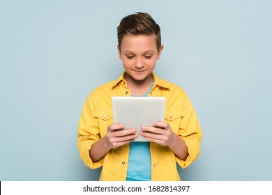 smiling and cute kid using digital tablet on blue background