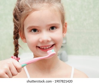 Smiling cute little girl brushing teeth in bathroom hygiene concept