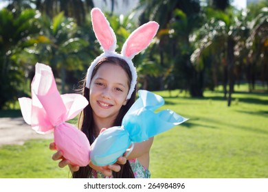 Smiling Cute Teen Girl With Rabbit Ears Holding Easter Chocolate Eggs In Colorful Paper In Park. Selective Focus On Face