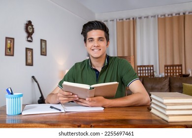 Smiling cute teenage boy studying with books - indoors stock photo. Royalty free image smart boy student teenage boy, sitting on chair, studying with books, at home - smiling face