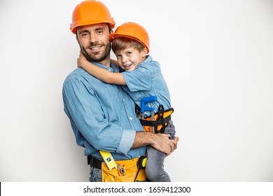 Smiling dad is holding boy on hands and hugging while they are wearing building helmets and belts with hand tools. Isolated on white background - Powered by Shutterstock