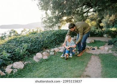 Smiling dad teaching little girl to ride a tricycle - Powered by Shutterstock