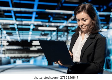Smiling data center computer scientist using laptop to configure mainframes hosting digital services. Cheerful server hub manager uses notebook device to repair equipment components