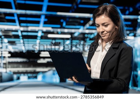 Smiling data center computer scientist using laptop to configure mainframes hosting digital services. Cheerful server hub manager uses notebook device to repair equipment components