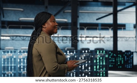 Smiling data center technician using tablet to manage software updates for system stability. Upbeat IT expert in server room configuring infrastructure with device for optimum performance, camera B