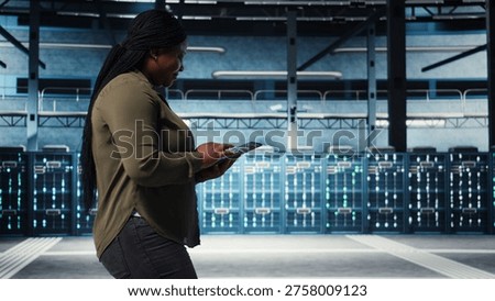 Smiling data center technician using tablet to manage software updates for system stability. Upbeat IT expert in server room configuring infrastructure with device for optimum performance, camera A
