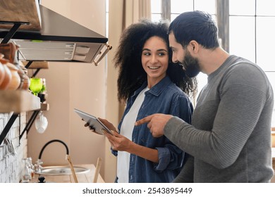 Smiling dating young mixed race couple using online app on tablet cooking together in home kitchen, ordering food delivery on supermarket store internet website, consulting recipe on Internet - Powered by Shutterstock