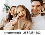 Smiling daughter eating cookie with her parents, enjoying a sweet treat together in the comfort of their home