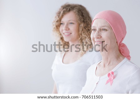 Smiling daughter supporting mother battling breast cancer wearing pink headscarf
