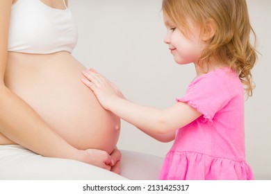 
Smiling Daughter Touching Pregnant Mother Big Belly With Hands And Waiting Future Brother Or Sister. Emotional Lovely Moment. Baby Expectation. Pregnancy Time. Closeup. Side View. Gray Background. 