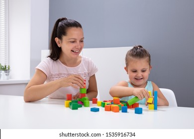 Smiling Daycare Worker Playing With Child Stacking Building Blocks On White Desk