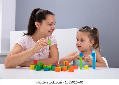 Smiling Daycare Worker Playing With Child Stacking Building Blocks On White Desk