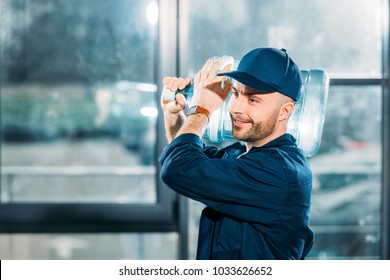 Smiling delivery man carrying water bottle on shoulder