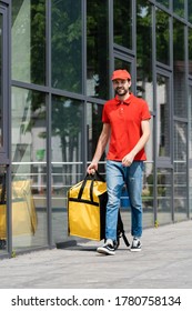 Smiling Delivery Man Holding Thermo Bag While Walking On Urban Street