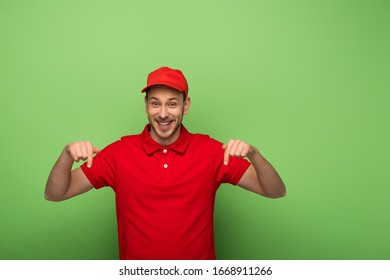 Smiling Delivery Man In Red Uniform Pointing With Finger Down On Green