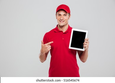 Smiling Delivery Man With Tablet In Studio. Isolated Gray Background