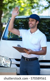 Smiling Delivery Man Waving Hand While Standing By Van