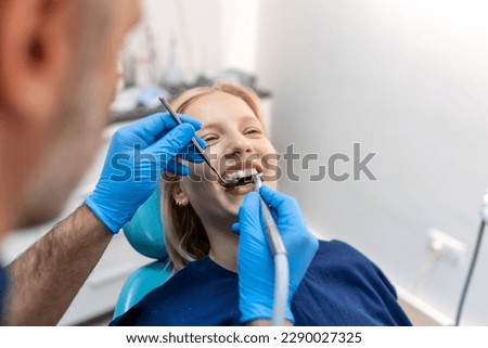 Smiling dentist communicating with young woman while checking her teeth during dental procedure at dentist's office.