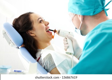 Smiling dentist holding an ultraviolet lamp and drying tooth filling of patient - Shutterstock ID 136867619