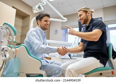 Smiling dentist shaking hand with male patient - Powered by Shutterstock