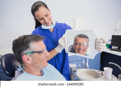 Smiling dentist showing teeth of her patient with a mirror in dental clinic - Powered by Shutterstock