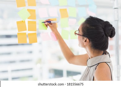 Smiling Designer Writing On Sticky Notes On Window In Creative Office