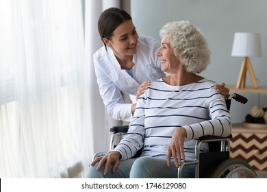 Smiling disabled elderly woman sitting in wheelchair talking with caring young nurse in living room, older generation receive homecare physical and moral support, caregiving and rehabilitation concept - Powered by Shutterstock