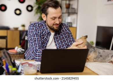 A Smiling Disabled Man Is Spending Time With His Dog During A Break At Work. In Front Of The Guy Is A Laptop And A Bunch Of Paperwork. Working At Home With Animals.