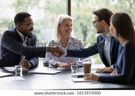 Smiling diverse businesspeople shake hands get acquainted greeting at team meeting in office. Happy multiracial male colleagues employees handshake at briefing with coworkers. Acquaintance concept.