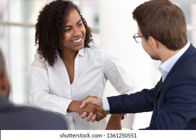 Smiling diverse businesswoman and businessman shake hands make partnership deal agreement at group office meeting negotiation thank for good teamwork expressing respect gender racial equality concept
