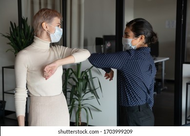 Smiling diverse female colleagues wearing protective face masks greeting bumping elbows at workplace, happy coworkers in medical facial covers protect from COVID-19 pandemics, healthcare concept - Shutterstock ID 1703999209